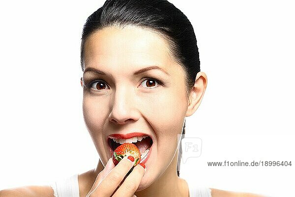 Schöne Frau mit sinnlichen roten Lippen ißt eine üppige reife rote frische Erdbeere mit ihren Lippen in Erwartung des Leckerbissen gescheitelt  Nahaufnahme von ihrem Gesicht vor weißem Hintergrund
