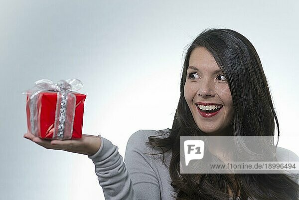 Schöne junge Frau  die ein dekoratives rotes Geschenk betrachtet  das sie in Aufregung und Vorfreude auf die Überraschung in ihrer Handfläche hält