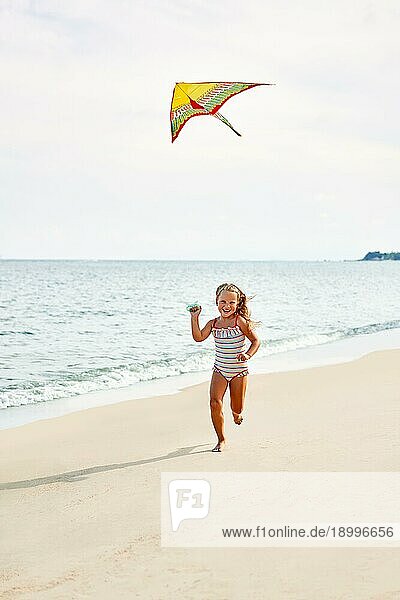 Glückliches Kind Mädchen mit einem Drachen läuft auf tropischen Strand. sorglose Kindheit Konzept