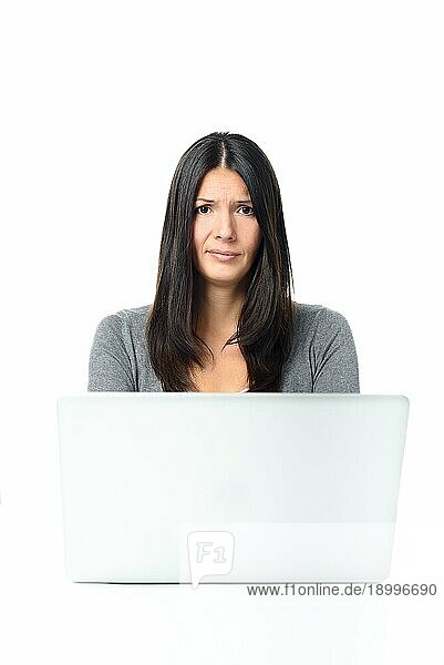 Skeptische junge Frau mit langen Haaren  die mit ihrem Laptop beschäftigt ist und in die Kamera schaut  vor weißem Hintergrund