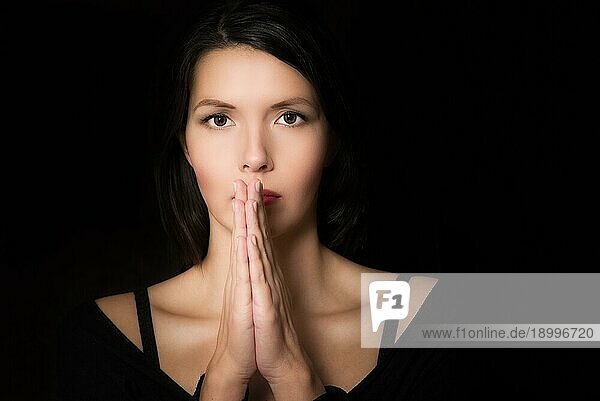 Dunkles  stimmungsvolles Porträt einer spirituellen jungen Frau  die mit gefalteten Händen und einem absichtlichen Blick betet
