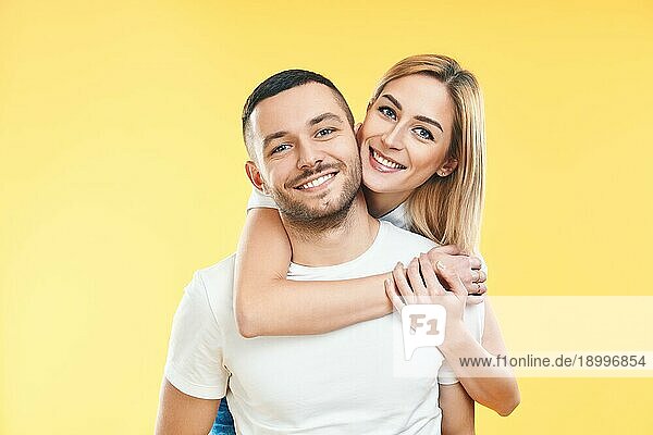 Glückliches  lächelndes  verliebtes Paar auf gelbem Hintergrund. Mann trägt seine Freundin Huckepack. Liebe  Romantik  Spaß Konzept