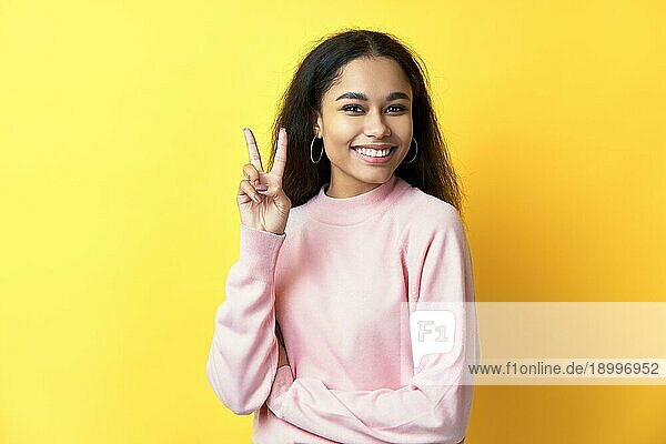 Glücklich lächelnde schwarze Frau macht Siegeszeichen auf gelbem Hintergrund. Friedenssymbol