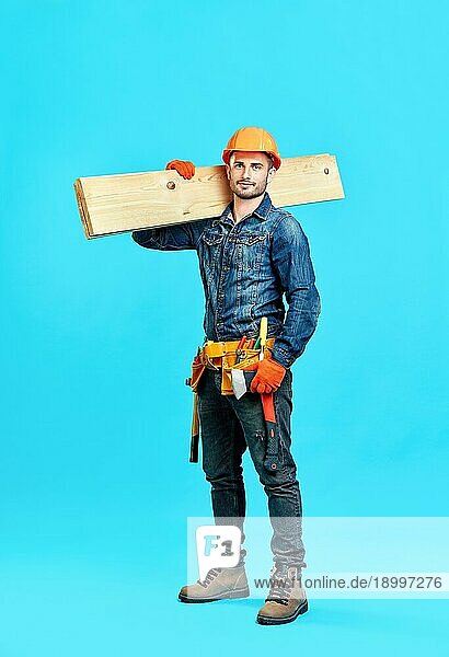 Ganzkörperporträt eines gutaussehenden männlichen Bauarbeiters  der einen Sicherheitshelm trägt  auf den Schultern über einem blaün Hintergrund  der zur Kamera schaut