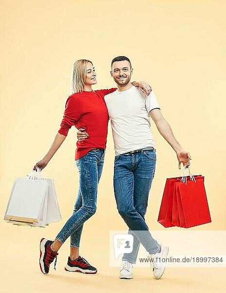 Porträt in voller Länge von jungen glücklichen Paar mit Einkaufstaschen in den Händen posieren über beige Hintergrund. Verkauf  shopaholic Konzept