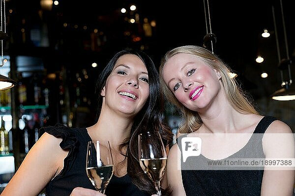 Zwei glückliche junge Freundinnen stoßen mit Champagner an  um ein besonderes Ereignis in einem Nachtclub zu feiern