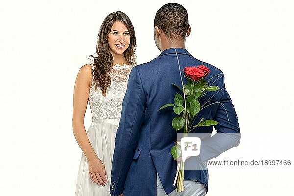 Stilvoller romantischer afrikanischer Mann mit einer roten Rose  die er hinter seinem Rücken versteckt  um seine attraktive lächelnde Geliebte am Valentinstag zu überraschen