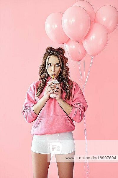 Trendy junge Frau trinkt Milchshake über rosa Luftballons Hintergrund. Kreativ  Feier  Pop Art Konzept