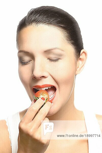 Schöne Frau mit sinnlichen roten Lippen ißt eine üppige reife rote frische Erdbeere mit ihren Lippen in Erwartung des Leckerbissen gescheitelt  Nahaufnahme von ihrem Gesicht vor weißem Hintergrund