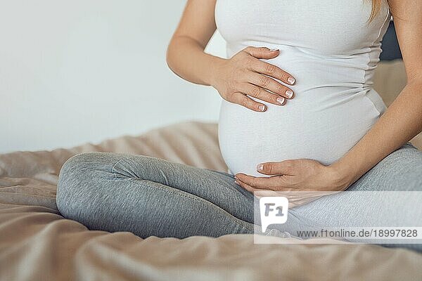 Junge schwangere Frau wiegt ihr Baby Beule oder Bauch mit ihren Händen in einer Nahaufnahme beschnitten Ansicht konzeptionelle der mütterlichen Liebe