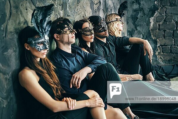 Gruppe von Freunden in Maskerade Karneval Maske sitzen auf dem Boden entspannen nach der Party. Schöne Frauen und Männer tragen venezianische Maske. Mode  Freunde Konzept