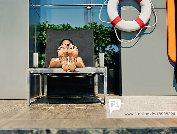 Junge schöne Frau entspannt sich auf einer Sonnenliege am Swimmingpool. Fokus auf Fuß