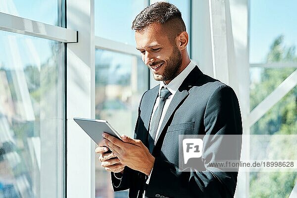 Junger lächelnder Geschäftsmann arbeitet an einem Tablet in einem modernen kreativen Büro. Business Technologie