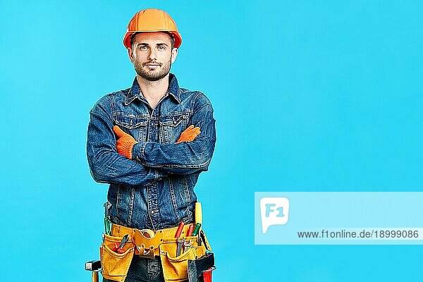 Porträt eines selbstbewussten  gut aussehenden männlichen Bauarbeiters mit verschränkten Armen und Kopierraum  der auf einem blaün Hintergrund steht und zur Kamera schaut