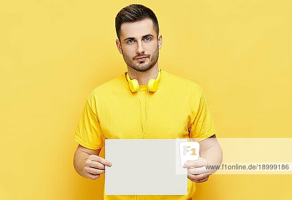 Junger kaukasischer Mann hält weiße leere Karte mit Platz für Text auf gelbem Hintergrund