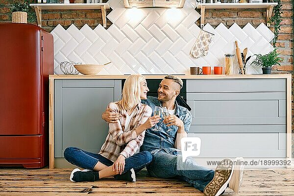 Romantische glückliches Paar sitzt auf dem Boden in der Küche und Toasting Champagner Gläser. Beziehung  Feier  Dating Konzept