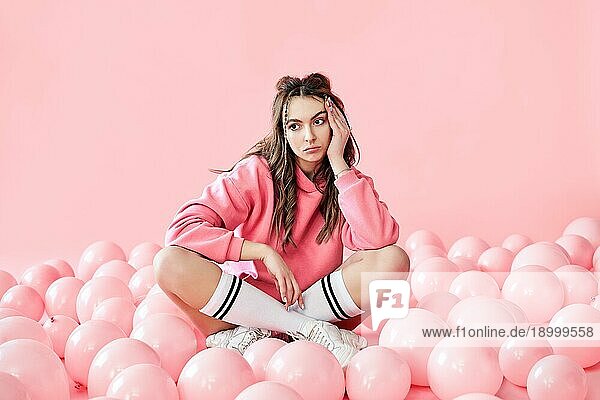 Bored modische Frau sitzt auf dem Boden mit rosa Luftballons auf rosa Pastell Hintergrund. Feiern  schlechte Party  Enttäuschung Konzept