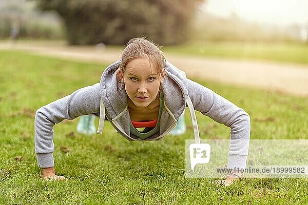 Sportliche junge Frau lächelt in die Kamera  während sie im Park Liegestützübungen macht