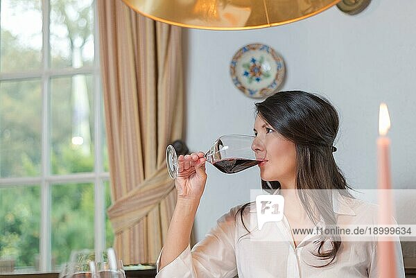 Attraktive junge brünette Frau trinkt ein Glas Rotwein und schaut nach links von der Kamera weg