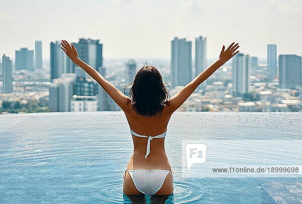 Zurück Blick auf glückliche Freiheit Frau mit erhobenen Armen genießen ihren Sommerurlaub am Swimmingpool auf dem Dach des Hotels. Reisen  Urlaub  Erfolg Konzept