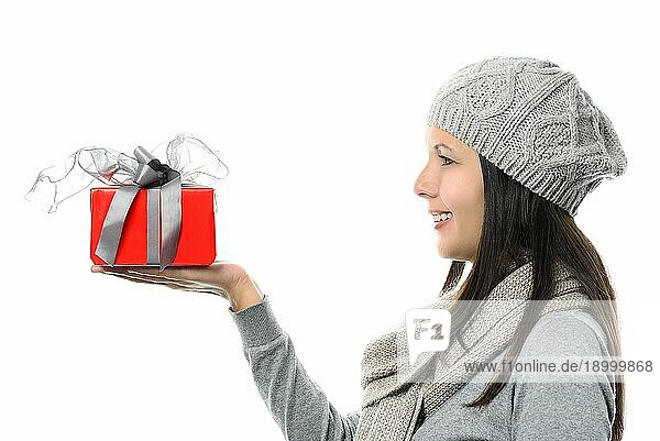 Close up Lächelnde Frau mittleren Alters in Seitenansicht trägt graue Wintermode zeigt kleine rote Geschenk auf der Hand  vor weißem Hintergrund