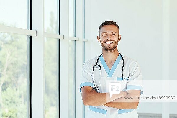 Porträt eines zuversichtlich lächelnden männlichen Arztes mit Stethoskop in medizinischer Uniform mit verschränkten Armen