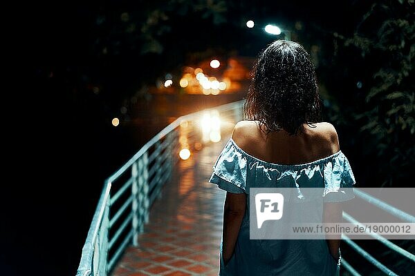 Rückenansicht einer jungen einsamen Frau  die nachts auf der Brücke spazieren geht