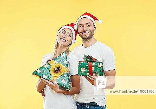 Junges glückliches Paar mit Weihnachtsgeschenkboxen auf gelbem Hintergrund. Geschenk  Urlaub  Feier Konzept