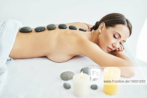 Junge Frau entspannt sich im SpaSalon mit heißen Steinen auf dem Rücken. Massage  Therapie  Schönheitsbehandlung Konzept