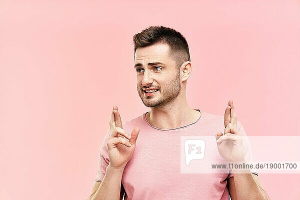 Junge gut aussehende Mann kreuzt ihre Finger und wünschen für viel Glück über rosa Hintergrund. Hoffnung und Wunsch Konzept