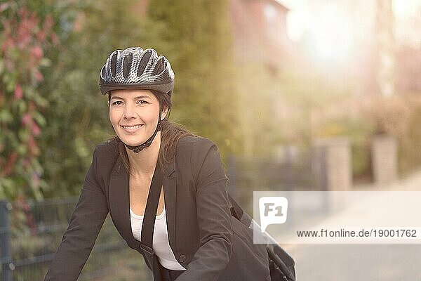 Glückliche junge Geschäftsfrau Radfahren auf der Straße mit Kopfbedeckung Going to her Office  Blick in die Kamera