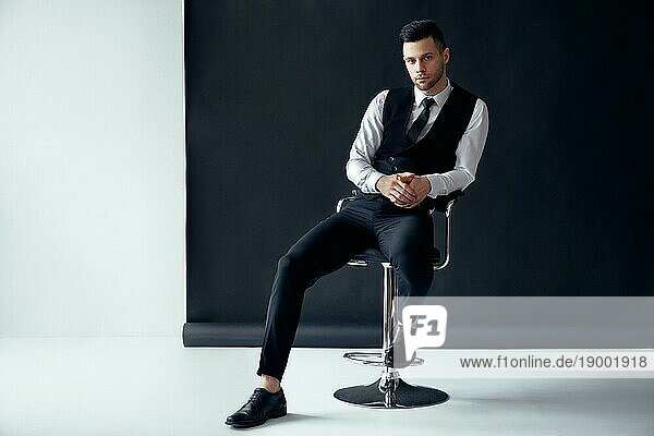 Elegante zuversichtlich Mann posiert und sitzt auf Stuhl auf schwarzem und weißem Hintergrund. Erfolg Konzept