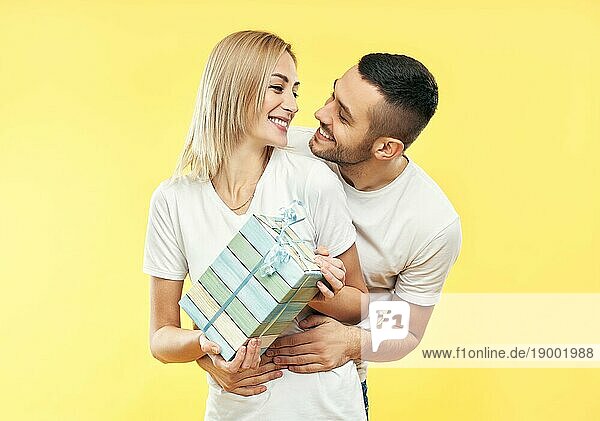 Junges glückliches Paar mit Geschenkbox auf gelbem Hintergrund. Geschenk  Urlaub  Feier Konzept