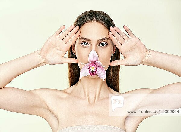 Schöne junge Frau mit Orchidee in ihrem Mund machen lustige Gesichter auf Studio Hintergrund. Weibliche Schönheit  Spa  saubere Haut Konzept