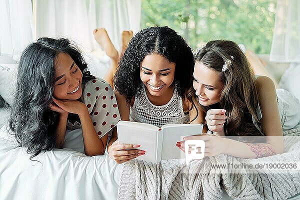 Lächelnde multiethnische Mädchen haben Spaß zusammen  Buch lesen und genießen Sie zu Hause Partei im Inneren des Wohnmobils. Frauen Freundschaft und Frauen Schönheit Konzept