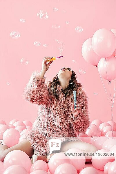 Junge hübsche Frau bläst Seifenblasen auf rosa Hintergrund mit Luftballons. Party  Feier  Spaß Konzept