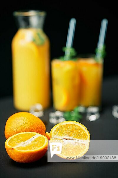 Leckerer frischer Orangensaft mit Eis  Minze und Früchten auf schwarzem Tischhintergrund. Fokus auf Früchte. Party  Getränk  Gesundheit Konzept