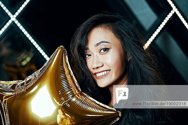 Porträt einer hübschen lächelnden asiatischen Frau  die Spaß hat und einen goldenen Luftballon hält. Party Zeit  Feier Konzept