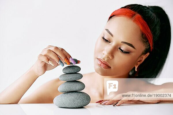 Hübsche afroamerikanische Frau macht Pyramide der Steine auf weißem Hintergrund. Balance Konzept