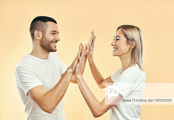 Porträt eines jungen lächelnden Paares  das sich gegenseitig High Five gibt  vor einem Studiohintergrund. Mann und Frau spielen Flammkuchen
