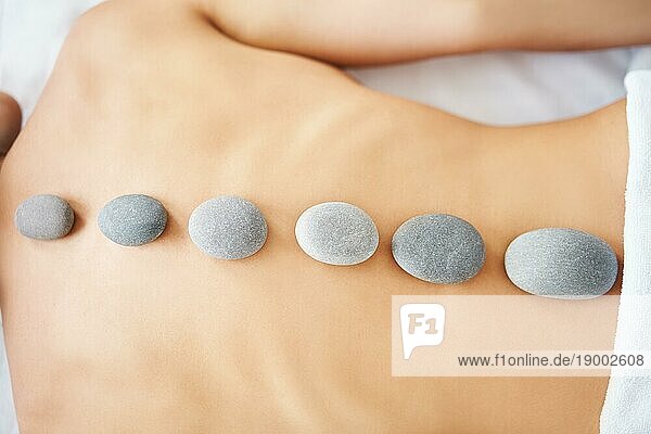 Abgeschnittene Nahaufnahme einer Frau  die sich in einem SpaSalon mit heißen Steinen auf dem Rücken entspannt. Massage  Therapie  Schönheitsbehandlung Konzept. Ansicht von oben