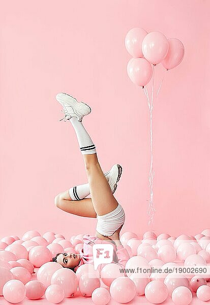 Junge hübsche Frau haben Spaß mit den Beinen nach oben in rosa Ballons über rosa Pastell Hintergrund liegen. lustige kreative Konzept