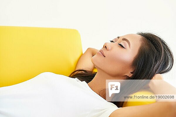 Junge hübsche Frau schloß die Augen auf dem gelben Sofa liegen und entspannen nach einem anstrengenden Tag. Ruhe  Komfort Konzept