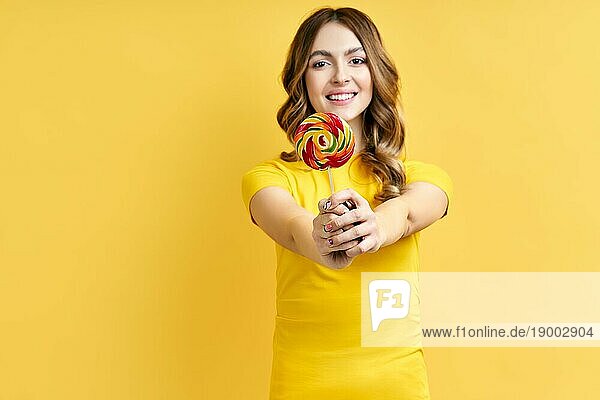Glückliche schöne Frau mit bunten Lutscher vorgelbem Hintergrund  Fokus auf Süßigkeiten