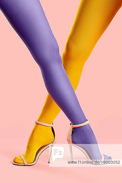 Lange schlanke gekreuzte Beine junger Frauen in gelben und lila Strumpfhosen posieren auf rosa Hintergrund. Pop Art  weibliches Konzept