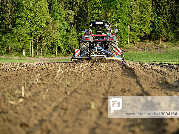Farmer leveling soil using tractor in farm at sunrise
