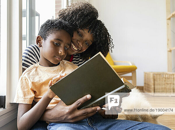 Smiling mother and son reading book together at home