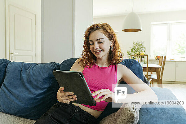 Happy young woman using tablet PC on sofa at home