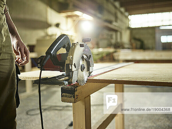 Carpenter with circular saw on oriented strand board in workshop