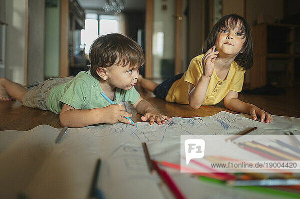 Brothers drawing with colored pencils lying on floor at home